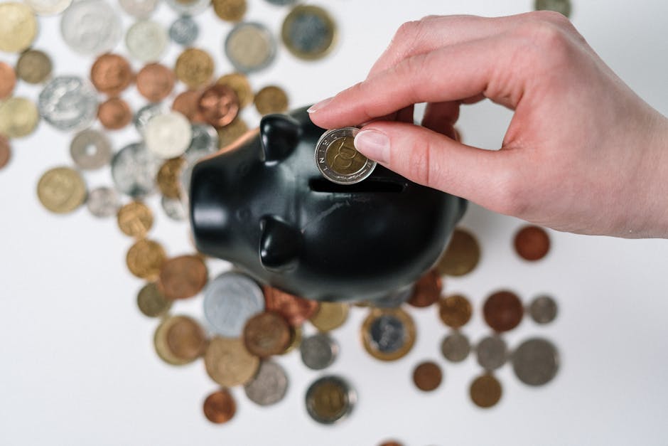 Close-up of a hand inserting a coin into a black piggy bank with scattered coins on a white background